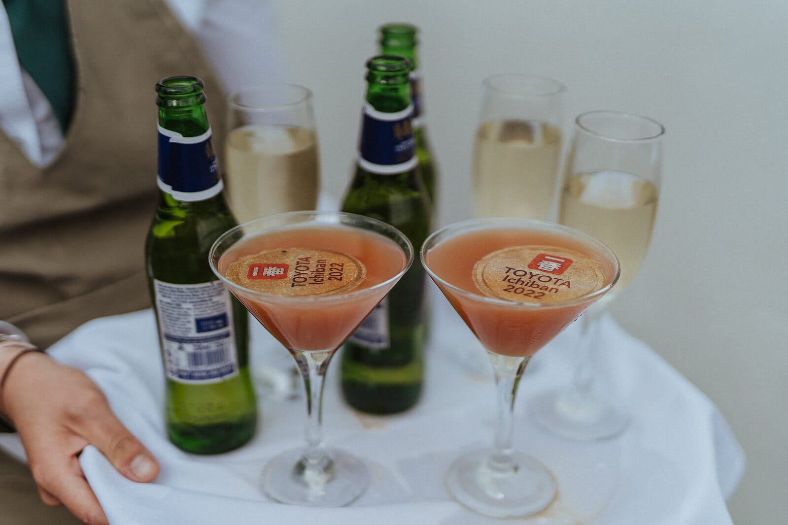 A waiter is holding two glasses of wine and a bottle of champagne to celebrate Jon Roe Toyota marking 50 years in business and receiving the Ichiban Award.